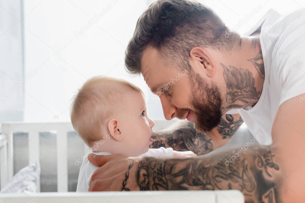 side view of young tattooed man and infant son looking at each other face to face