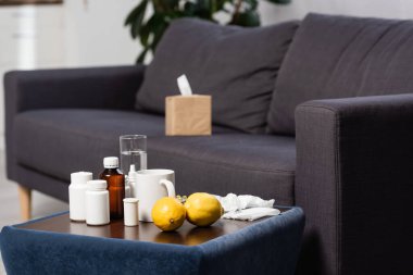 selective focus of medicines, fresh lemons and drinks on bedside table near grey sofa with paper napkins clipart