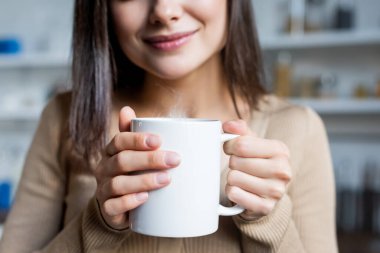 cropped view of pleased young woman holding cup of warm drink at home clipart