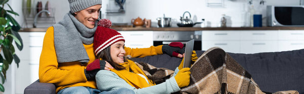 horizontal concept of excited couple in warm hats and gloves watching movie on laptop in cold kitchen