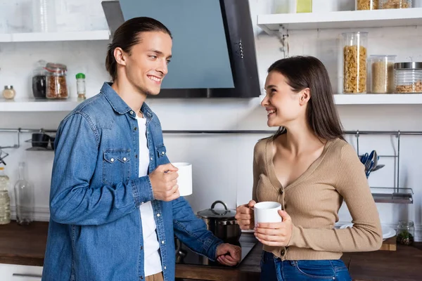 Alegre Casal Olhando Para Outro Enquanto Com Xícaras Café Cozinha — Fotografia de Stock