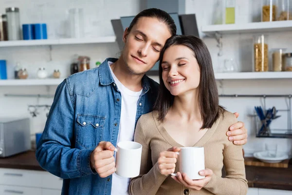 Pleased Couple Standing Kitchen Closed Eyes While Holding Cups Coffee — Stock Photo, Image