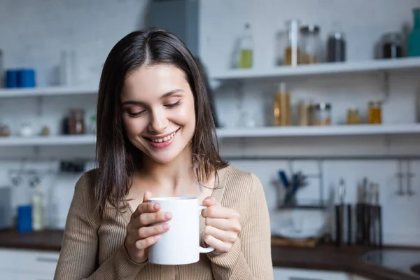 嬉しい若い女性がキッチンで温かいお茶を持っていて — ストック写真