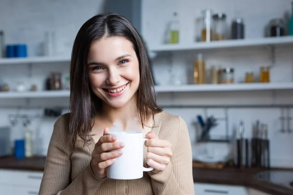 Mujer Alegre Mirando Cámara Mientras Sostiene Taza Bebida Caliente Casa —  Fotos de Stock