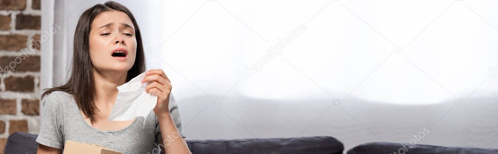 panoramic crop of sick woman sneezing while holding paper napkin at home