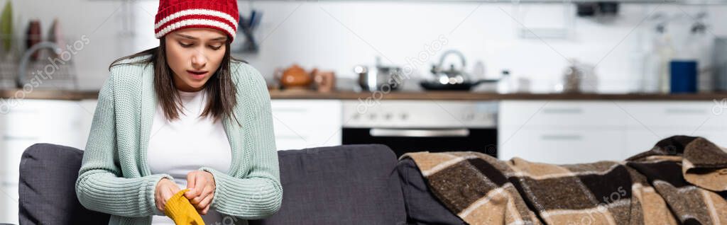 Website header of freezing woman in knitted hat putting on warm gloves while sitting on sofa in cold kitchen — Stock Image Website Header Freezing Woman Knitted Hat Putting Warm Gloves While Royalty Free Stock Photos