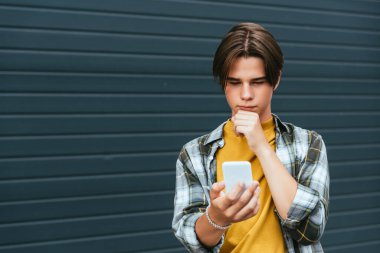 Pensive teenager using smartphone near building outdoors  clipart
