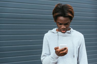 Afro-Amerikan ergen dışarıda akıllı telefon kullanıyor. 