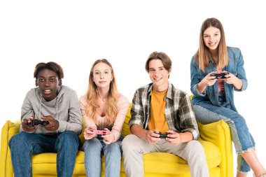 KYIV, UKRAINE - 21 AĞUSTOS 2020: Beyazlar üzerinde izole edilmiş kanepede video oyunu oynayan pozitif çok ırklı gençler