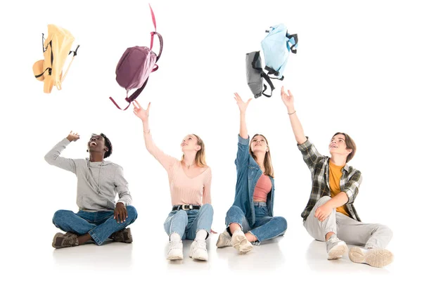 Adolescentes Multiétnicos Positivos Jogando Mochilas Enquanto Sentados Fundo Branco — Fotografia de Stock