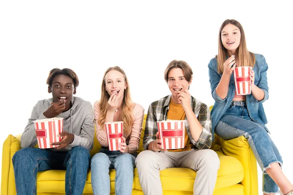 Wielokulturowi Przyjaciele Uśmiechnięci Podczas Jedzenia Popcornu Żółtej Kanapie Odizolowani Białym — Zdjęcie stockowe