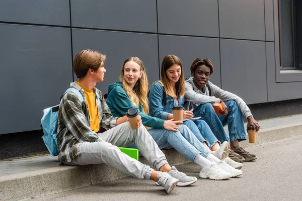 Pozitivní Multietnické Teenageři Kávou Jít Knihy Sedí Chodníku Blízkosti Budovy — Stock fotografie