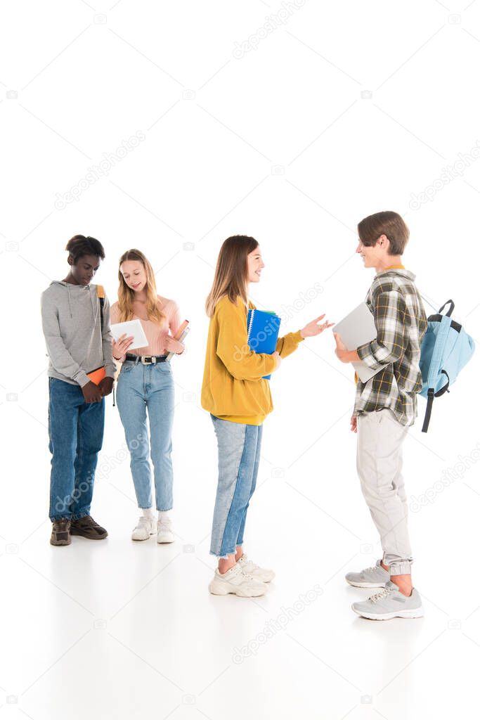 Selective focus of smiling teenagers with notebooks and gadgets talking on white background