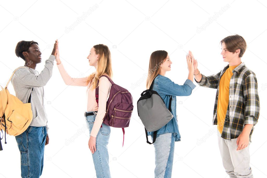 Smiling multiethnic teenagers with backpacks giving high five isolated on white