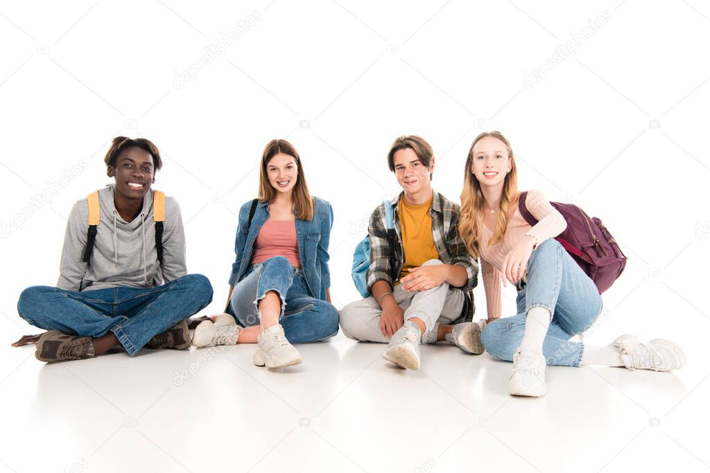 Smiling multicultural teenagers with backpacks looking at camera on white background