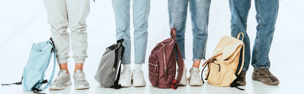 Panoramic crop of teenagers standing near backpacks on grey background