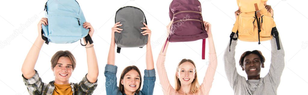 Panoramic shot of smiling multiethnic teenagers holding backpacks isolated on white