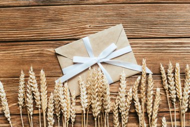 top view of envelope with bow near wheat ears on wooden background clipart
