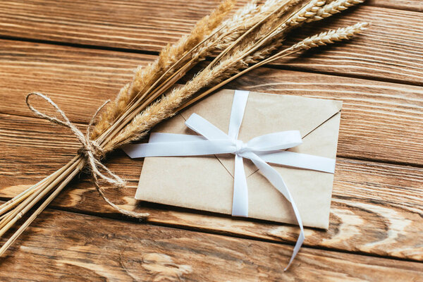 envelope with bow near wheat ears on wooden background