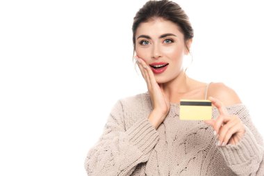 Moda süveter giyen heyecanlı bir kadın beyaz kameraya bakarken kredi kartı gösteriyor.