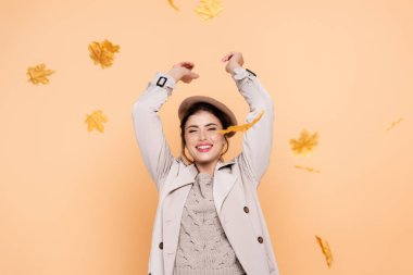 excited woman in trench coat and beret throwing yellow leaves on peach clipart