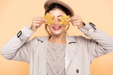 Şık trençkotlu ve bereli, sarı yapraklı, şeftali rengi gözleriyle neşeli bir kadın.
