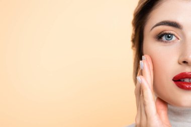 Şeftalide izole edilmiş kameraya bakarken yüzüne dokunan kırmızı dudaklı genç kadının portresi.