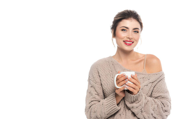 pleased woman in openwork sweater holding cup of warm beverage while looking at camera isolated on white