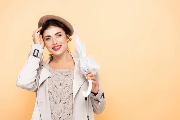 穿着秋装的时髦女人拿着折叠伞在桃子上摸贝雷帽 — 图库照片