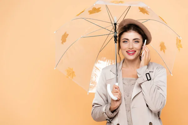 秋の流行の服を着た若い女性が秋の紅葉と傘の下でスマートフォンで話している — ストック写真