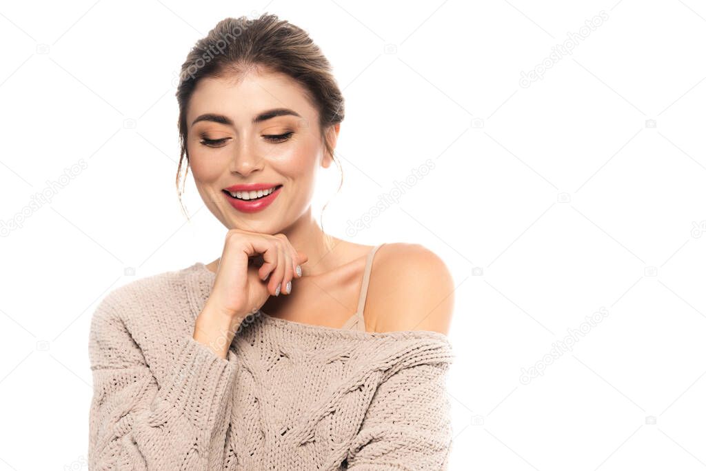 joyful woman in fashionable sweater posing with hand near chin isolated on white