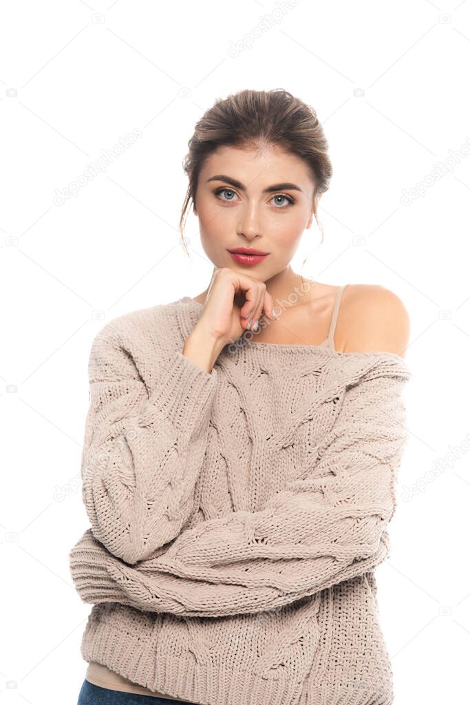 trendy woman in knitted sweater posing with hand near chin isolated on white