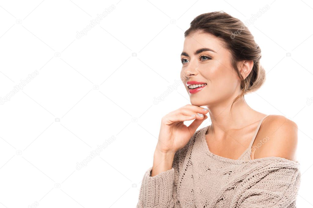 stylish woman in trendy sweater holding hand near chin while looking away isolated on white