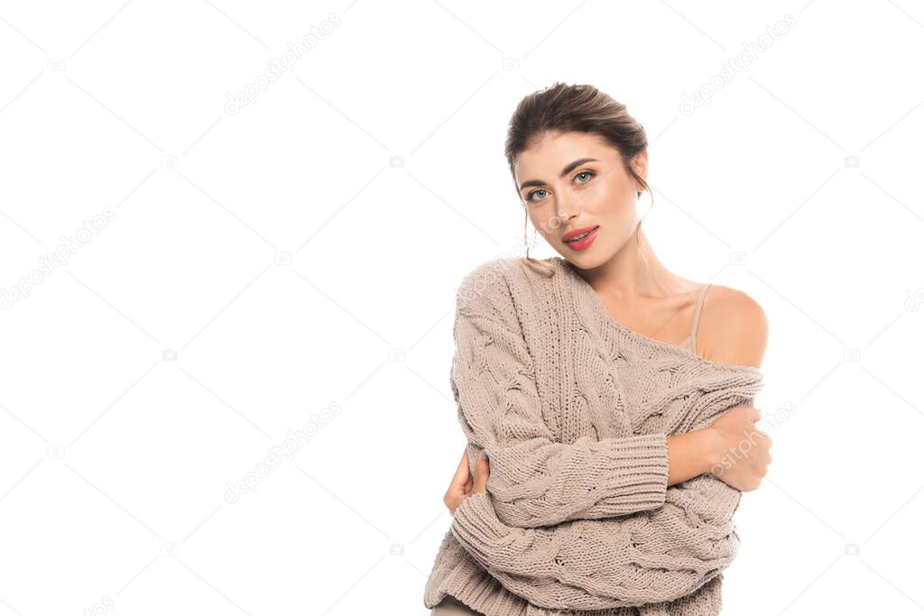 trendy woman in openwork sweater looking at camera while hugging herself isolated on white