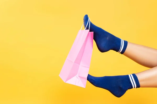 黄色の背景に隔離された靴下で女性の足にぶら下がっているピンクの紙袋のトリミングビュー — ストック写真