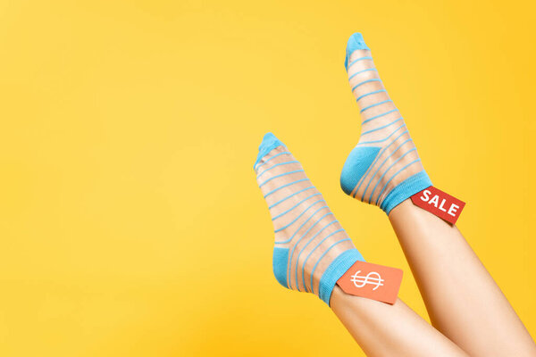 Cropped view of female legs in socks and tags with dollar symbol and sale word isolated on yellow