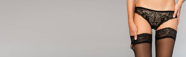 Сексуальная женщина в кружевном белье, держась за руку под чулком изолированы на сером, баннер