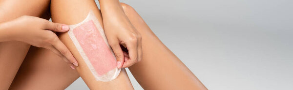 Close up view of woman removing wax stripe on smooth leg on grey, banner