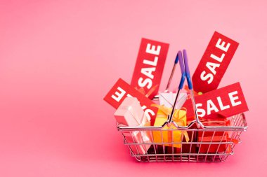 shopping basket with presents and red sale tags on pink  clipart