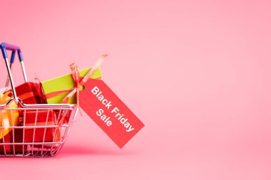 Hediyelerle dolu alışveriş sepeti ve üzerinde pembe, siyah cuma konsepti olan kırmızı etiket. 