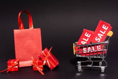 Alışveriş çantası ve oyuncak arabasının yanında siyah arka planda satış etiketleri olan hediyeler, Kara Cuma konsepti. 