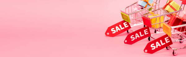 панорамный снимок подарков в торговых тележках с ярлыками продажи на розовый, черный пятница концепции 