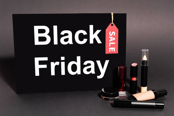 placard with black friday lettering near decorative cosmetics on dark background