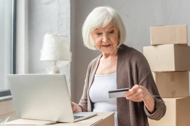 Kredi kartı ve dizüstü bilgisayarla online alışveriş yapan yaşlı bir kadın.