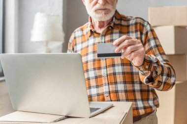 Kredi kartı ve dizüstü bilgisayarla online alışveriş yapan kıdemli adamın kısmi görüntüsü
