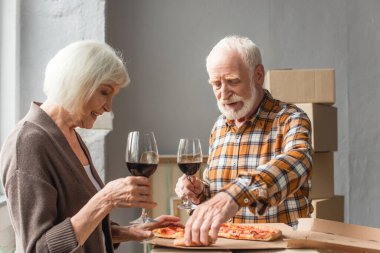 Şarap bardakları tutan yaşlı çift ve yeni evde pizza yiyen adam.