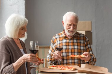 Son sınıf çifti yeni evde ellerinde pizza ve şarap kadehleri tutuyor.