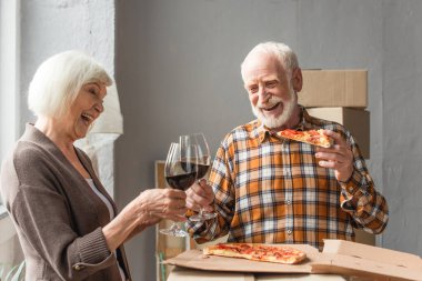 Gülen son sınıf öğrencisi elinde pizza ve yeni evinde karısıyla kadeh tokuşturuyor.