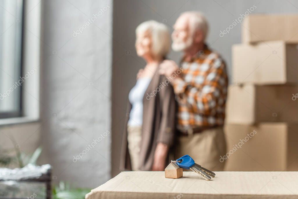 Blurred view of senior couple moving into new house and keys on foreground
