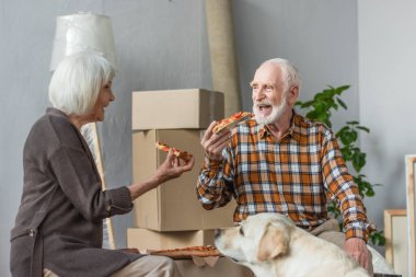 Yeni evde pizza yiyen son sınıf çifti ve yanında oturan köpek.